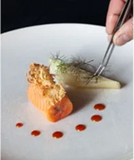 Le chef dressant à la pince une assiette de saumon